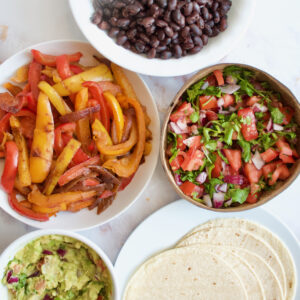 Taco spread including fajita peppers, black beans, tortillas, salsa and guacamole