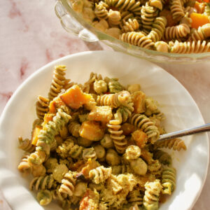 Serving dish of pesto pasta with a bowl of served pasta