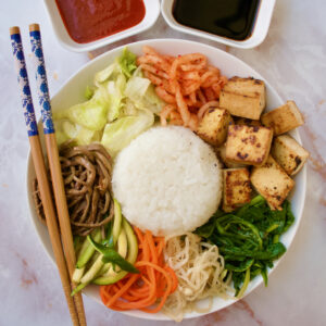 A bibimbap bowl with tofu, spinach, beansprouts, carrots, zucchini, frenbrake, kimchi and lettuce