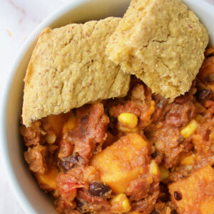 A bowl of sweet potato chilli with two pieces of cornbread