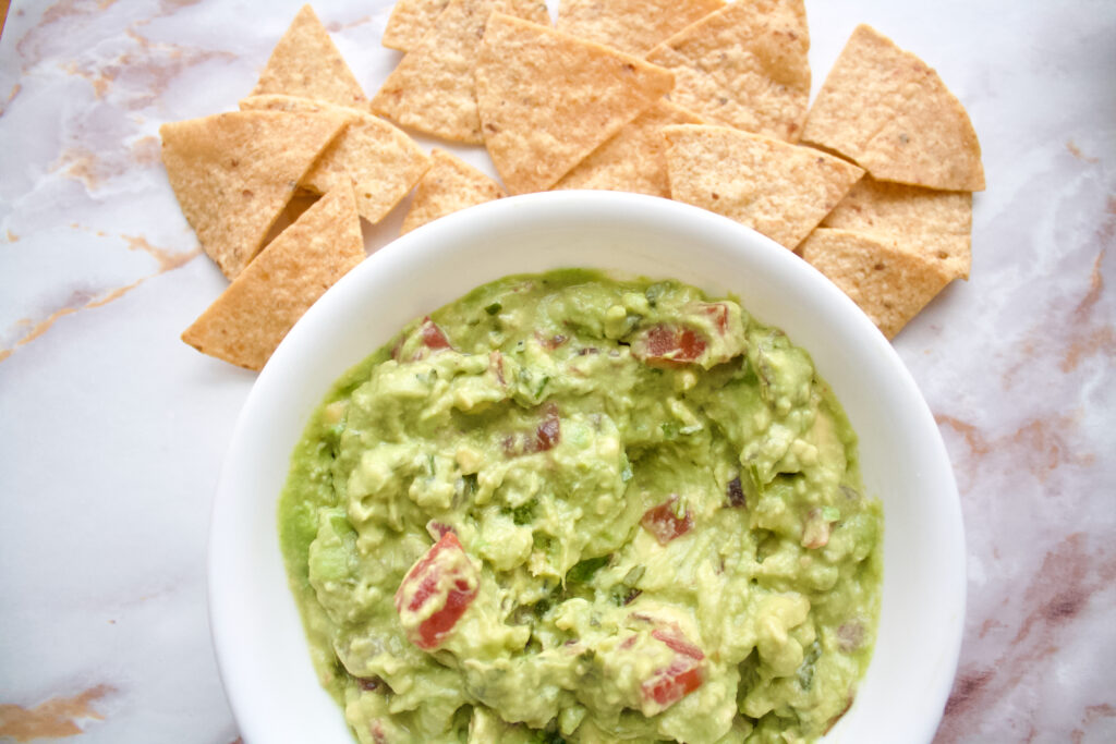 A bowl of vegan guac with corn tortilla chips spread around
